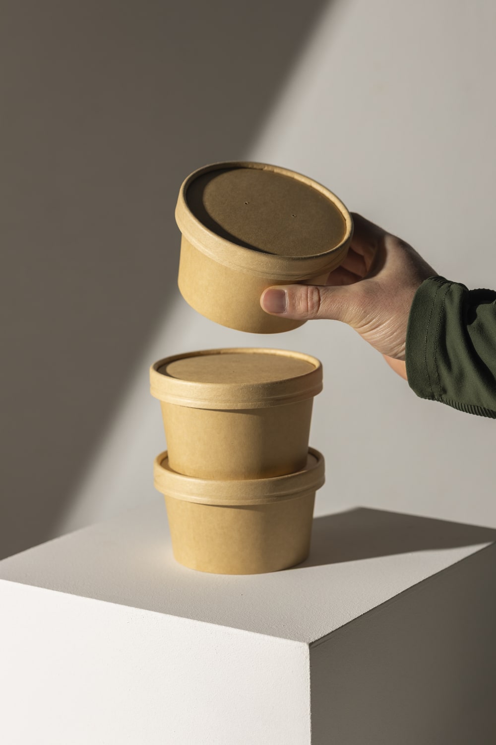 Yucca Packaging kraft soup tub and lids on a white pedestal with a creamy background.